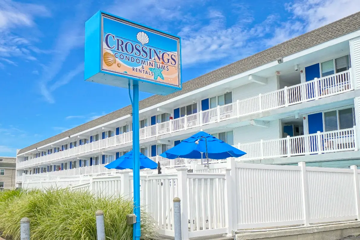 The Crossings sign in front of the three-story white building, with blue umbrellas behind a white picket fence